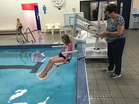 young person and adult using a hydraulic lift to enter water in the Pictou Pool